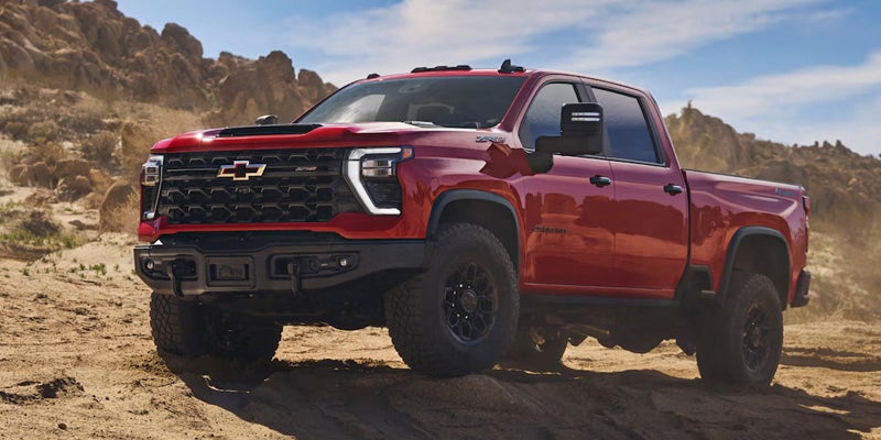 Red Chevrolet Silverado HD ZR2 parked on a sandy, rocky desert terrain.