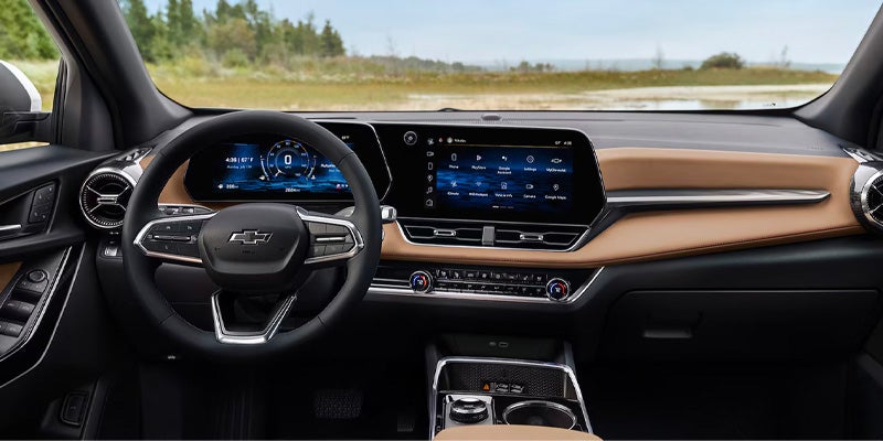 Interior of a Chevrolet car with tan dashboard, digital displays, and a view of a grassy landscape outside.