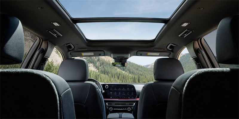 Interior view of a car with an open sunroof overlooking mountains and a forest through the windshield.
