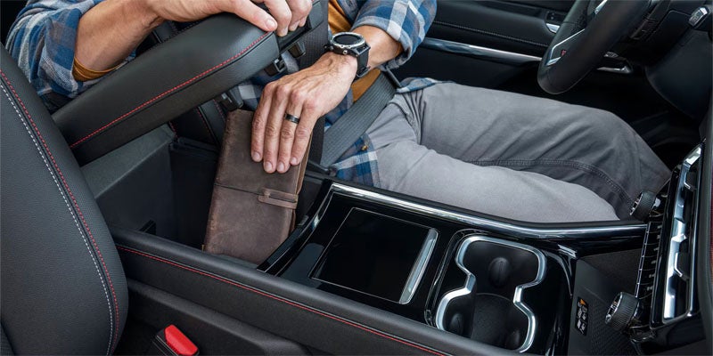 A person's hands placing a brown journal into the concealed middle storage compartment of a car's center console.