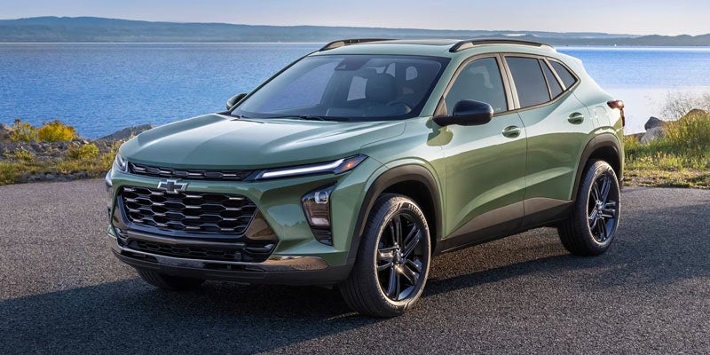 A new sage green Chevrolet Trax crossover SUV parked on an asphalt road next to a large blue lake.